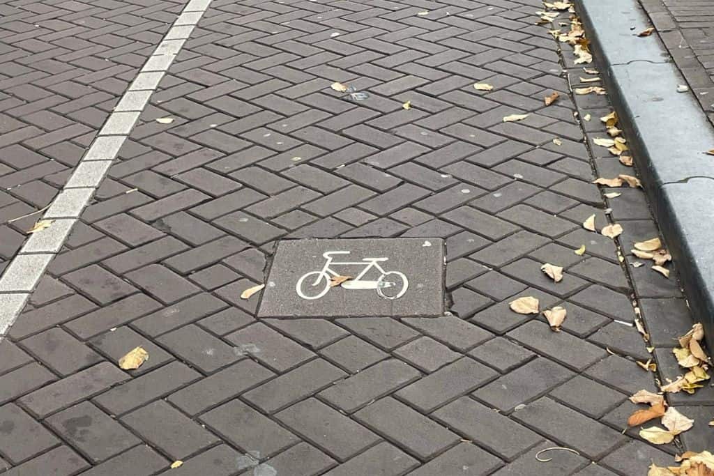 A white bike sign in a bike lane in Amsterdam. The bike is facing the way you should be biking in Amsterdam.