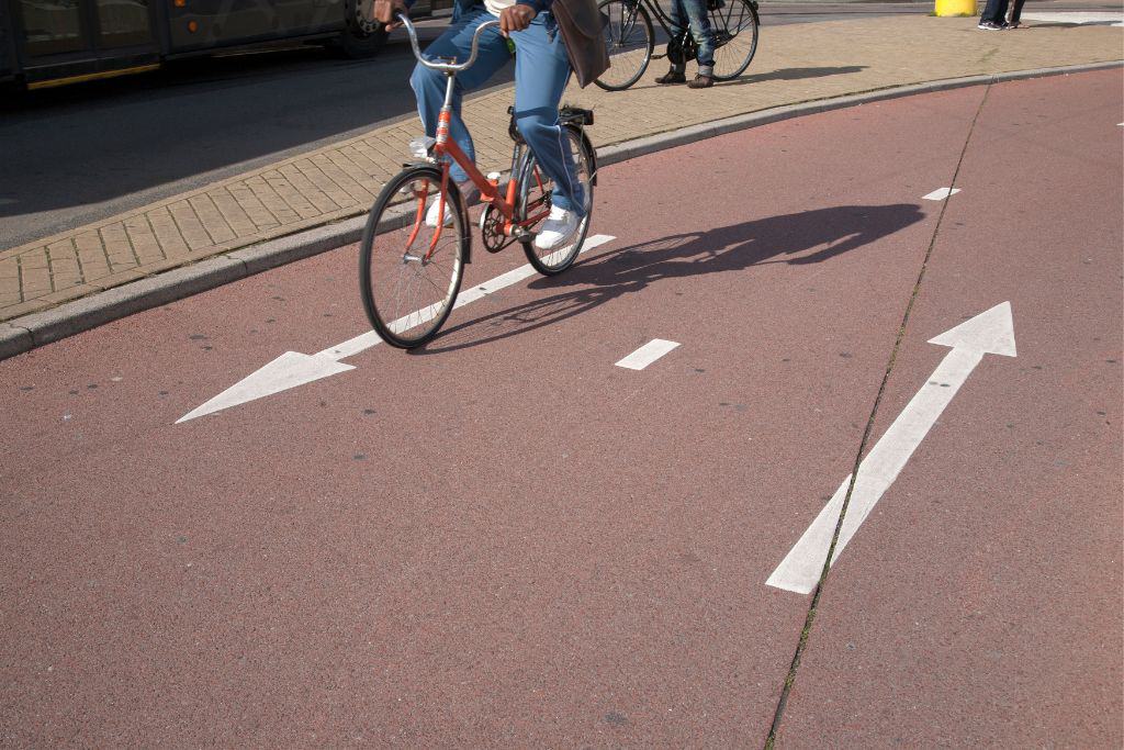 A bike lane in the Netherlands that is red in color and allows for two way traffic. Two arrows on the ground show the flow of traffic for a biker.