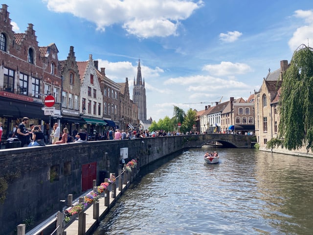 The beautiful waters on Bruges with a canal boat coming through the waters and passersby on the bridges.