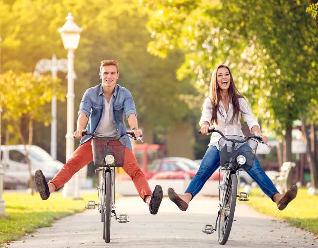 A couple riding two bikes with baskets in the fall in the late afternoon sunshine. They have taken their feet off the pedals. The best coupe travel quotes for instagram are inspired by moments like this.