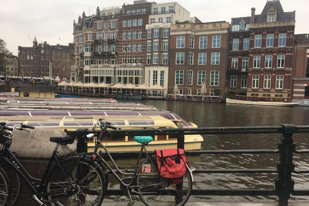Bikes along a canal in Amsterdam with houseboats and row homes in the background. 