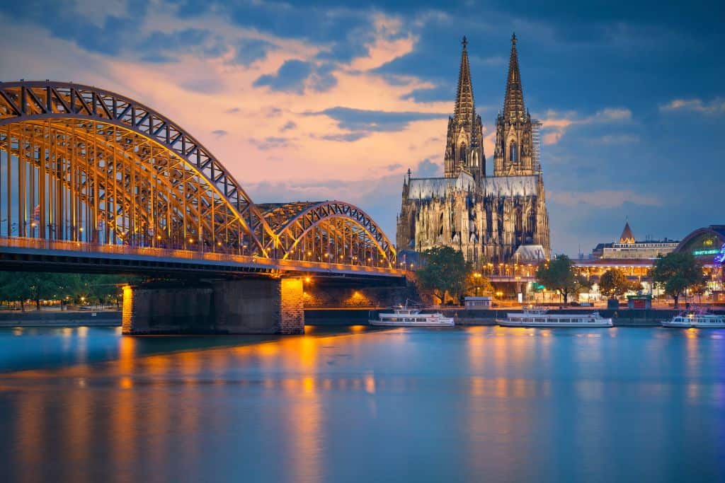 A view of the Cologne Cathedral at night with the water in the foreground.