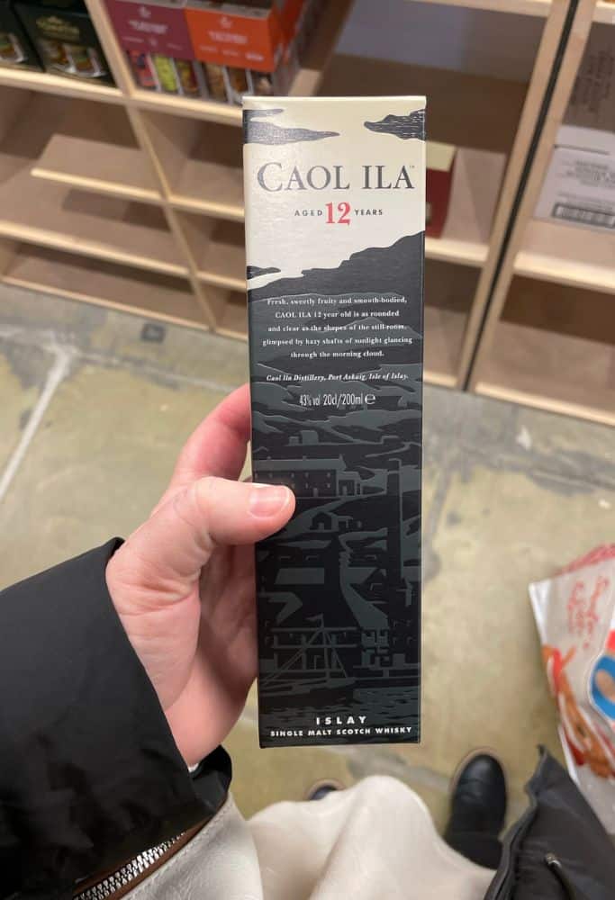 Scotland Souvenirs A person holds a box of Caol Ila 12-year-old single malt Scotch whisky in a shop. The sleek packaging highlights the whiskyโs origins from Islay, making it a great Scotland souvenir.