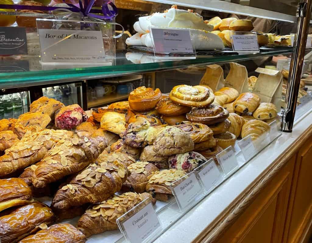 A bakery display case filled with an assortment of freshly baked pastries, including croissants, pain au chocolat, and fruit-filled Danish pastries. The treats are neatly arranged with small labels indicating their names and prices.