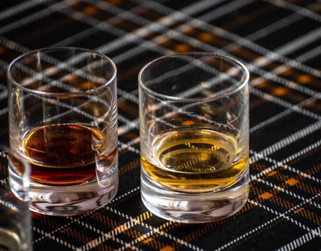 Whiskey tasting in Edinburgh, with two glasses of fine Scotch whiskey laid on a plaid cloth, highlighting the rich flavors and heritage on a top-rated food tour.