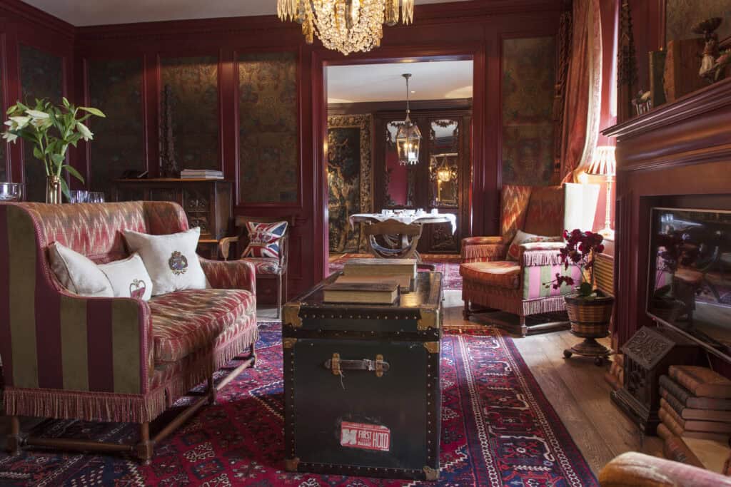 Historic Hotels in Edinburgh A hotel suite at The Witchery which exudes historic elegance. The room is decorated in deep red with a brocade couch and chair and an antique trunk as a cofee table. A fireplace is on the side and you can see through to a dining room set up for dinner in the other room.
