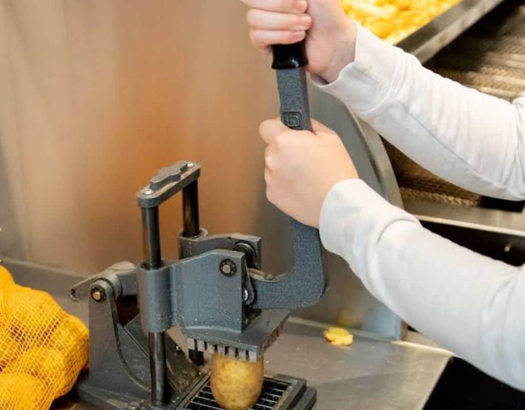A close-up of hands using a potato cutter in a fry shop, slicing fresh potatoes into thick-cut fries before frying. Freshly cut potatoes are key to making the perfect french fries in Amsterdam.
