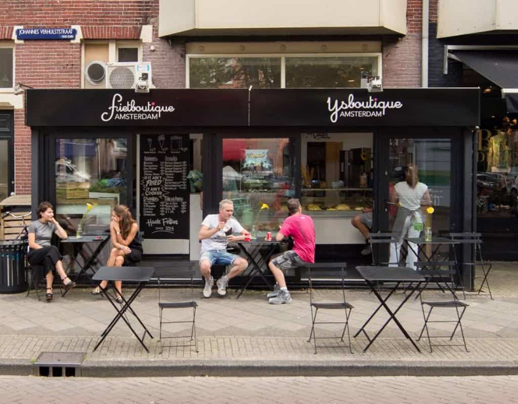 The exterior of Fritboutique Amsterdam, a modern fry shop with people sitting at outdoor tables enjoying their food. A trendy spot to try gourmet French Fries in Amsterdam.