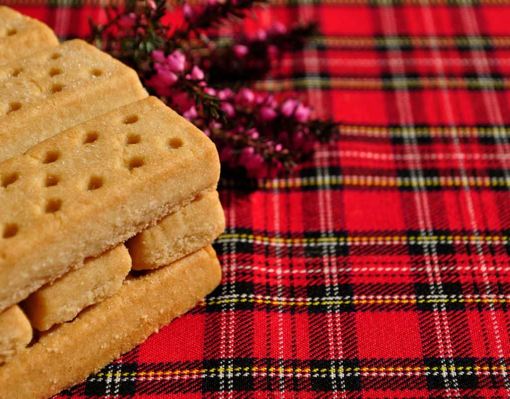 Scottish shortbread fingers stacked on a vibrant red tartan cloth, a tasty treat often brought home as one of the top Edinburgh souvenirs.