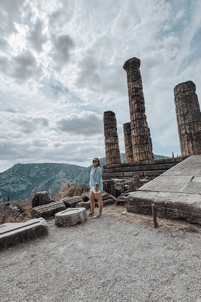 Best eSIM for Europe Woman standing at the Temple of Apollo ruins in Delphi, Greece, with ancient stone columns and mountain views, showcasing travel connectivity using Simlocal eSIM. Ideal for illustrating the best eSIM for Europe in a Simlocal eSIM review.