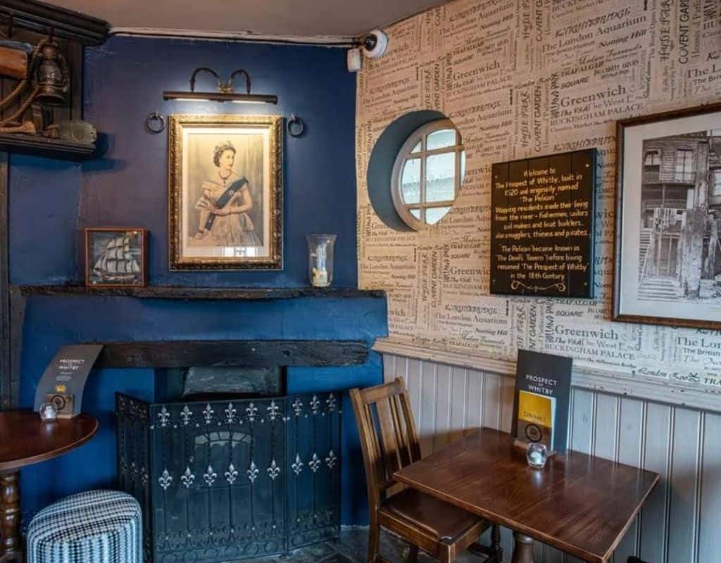 Cozy blue-painted pub corner with a small fireplace, framed historical portraits, nautical artwork, and intimate wooden tables reflecting the charm of London Oldest Pubs.