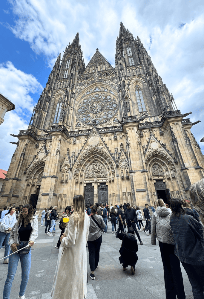 Crowds gathering outside the towering Gothic façade of St. Vitus Cathedral inside Prague Castle, showcasing detailed stone carvings and soaring spires.