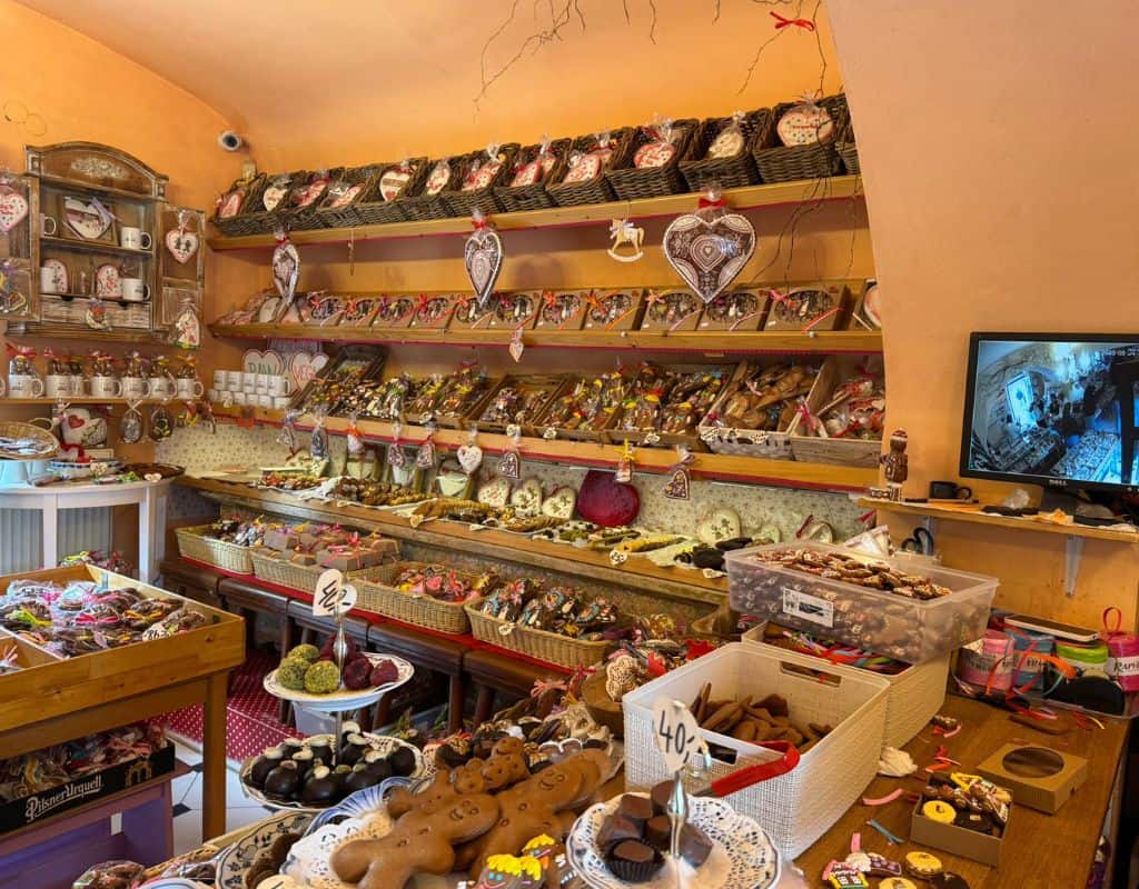 Cozy Prague gift shop filled with decorated gingerbread cookies, handmade sweets, baskets, and traditional Czech souvenirs lining wooden shelves.