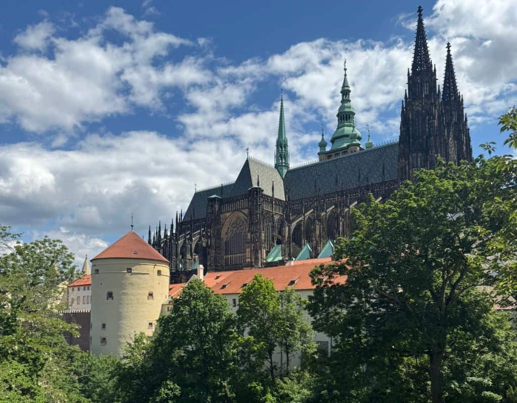 St. Vitus Cathedral rising above Prague Castle with Gothic towers, green copper spires, and historic castle buildings framed by trees during 3 Days in Prague.