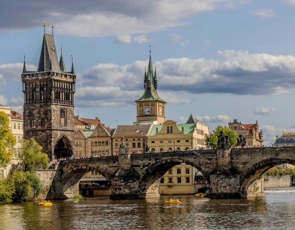 Charles Bridge crossing the Vltava River with historic stone towers, statues, and Prague’s skyline stretching behind the riverfront.