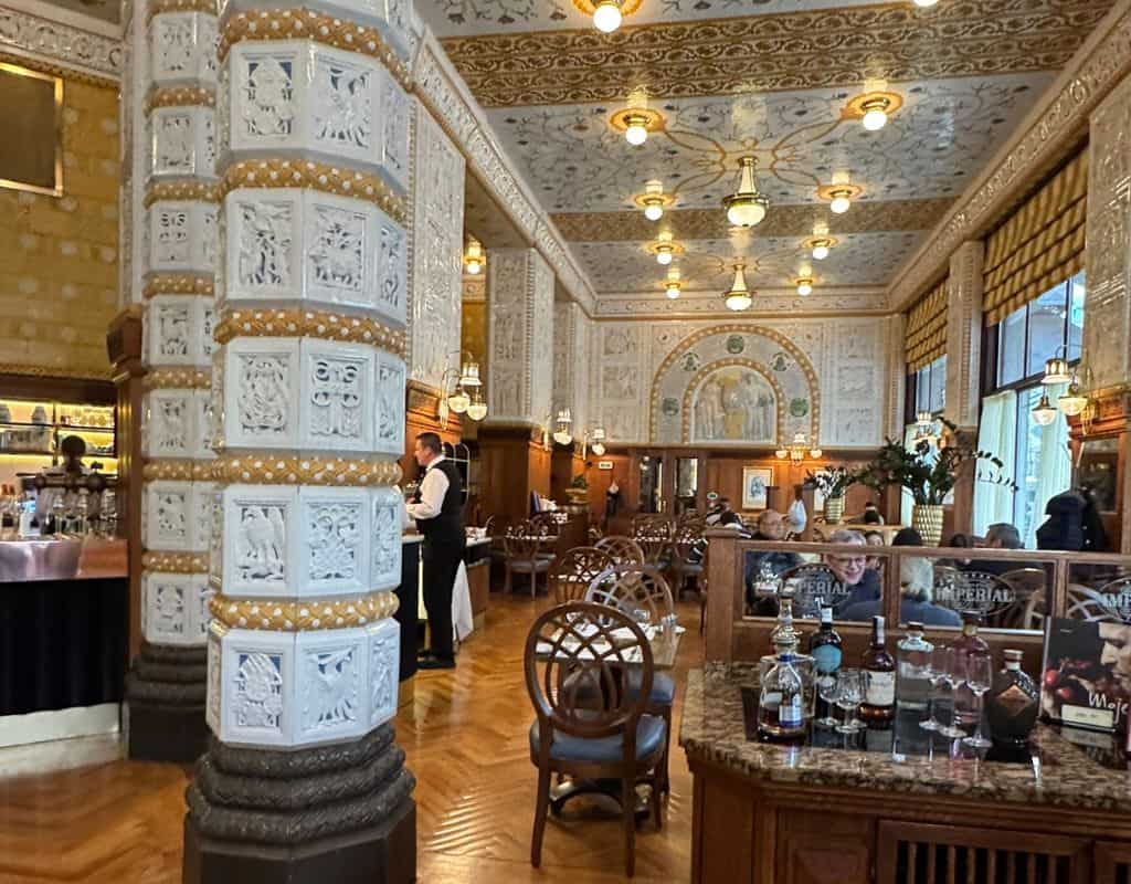 Elegant interior of Prague’s Café Imperial featuring ornate ceramic columns, decorative ceilings, chandeliers, and classic Art Deco architecture.