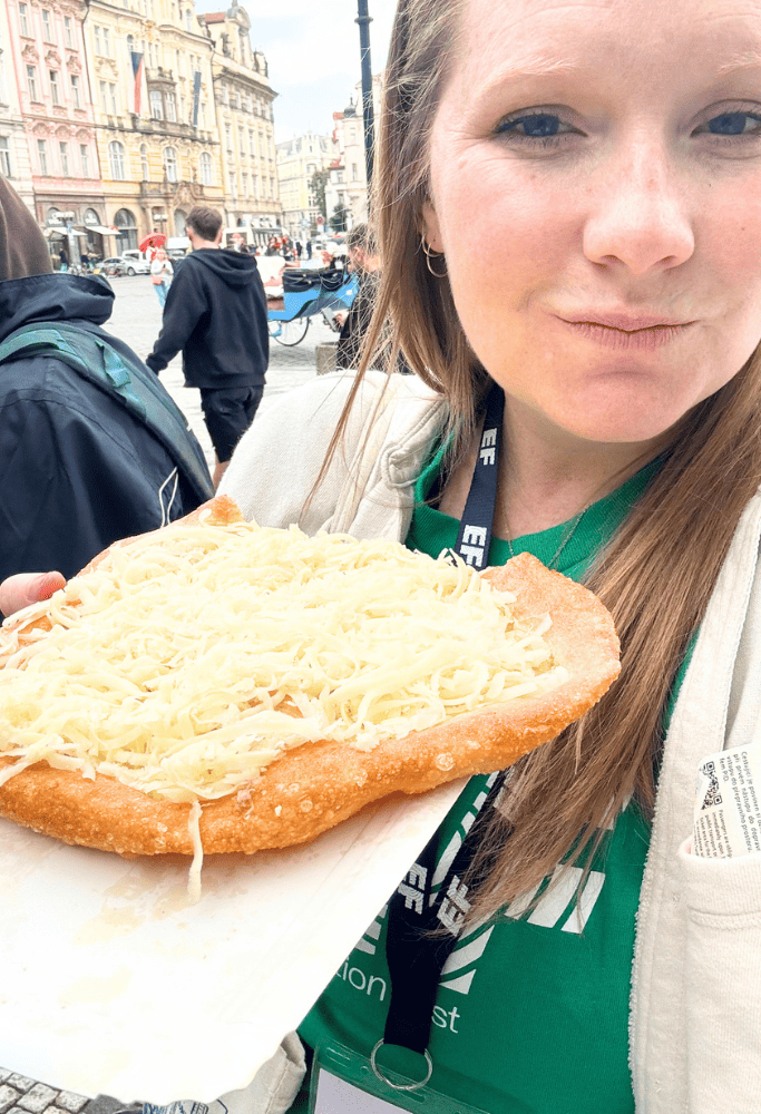 Taylor holding traditional Czech fried bread topped with melted cheese while exploring Prague’s historic city center.