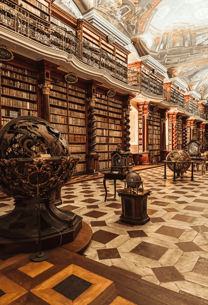 Historic library interior at Prague’s Clementinum featuring ornate frescoed ceilings, antique globes, marble floors, and floor-to-ceiling bookshelves.
